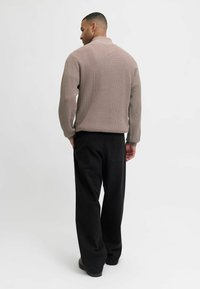 Suéter de punto en beige claro con un patrón texturizado, combinado con pantalones negros de pierna ancha. Detalles visibles en el cuello y la costura trasera.