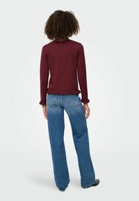 Bourgogne långärmad topp med volangsläpp, kombinerad med ljus tvättade vida jeans. Texturerad tyg, avslappnad passform och subtila detaljer vid ärmarna.