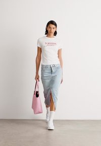 Hvit t-skjorte med rødt "tommy"-logo, lyseblå denimskjørt med sideløsning, rosa håndveske og hvite sneakers. Glatte teksturer, uformell stil.