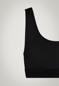Top sportivo nero caratterizzato da una texture liscia, spalline larghe e una fascia di supporto alla base con un sottile dettaglio di branding.