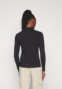 Svart långärmad polo med krage, slim fit, mjukt tyg och platta sömmar. Bärs med beiga cargobyxor.