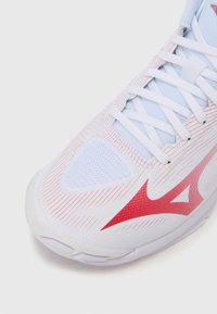 Λευκό αθλητικό παπούτσι με κόκκινες λεπτομέρειες, με ανάγλυφο επάνω μέρος από ύφασμα δικτύου, μυτερό σχέδιο, επίπεδα κορδόνια και καουτσουκένια εξωτερική σόλα με ανάγλυφα αυλάκια.