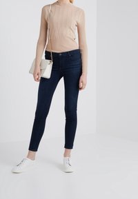 Ljusbeige ribbad långärmad topp som matchas med mörkblå slim-fit jeans och vita sneakers. Toppen har ett subtilt diamantmönster.