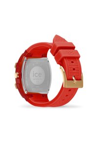 Reloj de silicona roja con caja cuadrada; herrajes en tono dorado, correa texturizada y parte trasera de metal que muestra detalles de la marca y el movimiento. Resistente al agua hasta 5ATM.