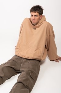 Hanorac bej supradimensionat cu un buzunar frontal și detalii cu logo, asortat cu pantaloni cargo verzi măslinii cu multiple buzunare.