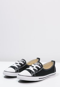 Svarta canvas sneakers med vita gummitåspetsar, kontrasterande söm, snörning framtill och en låg profil med en grårandig sula.