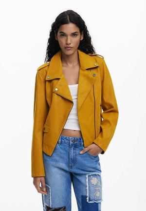 Yellow leather biker jacket with a lapel collar, zippered pockets, and button accents, paired with light blue distressed jeans.