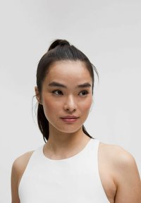 Haut sans manches blanc avec un col montant, texture lisse et coupe ajustée. Cheveux en queue de cheval haute, arrière-plan neutre.