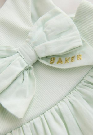 Vaaleanvihreä ribbineulosta kangas, jossa suuri yhteen sopiva rusetti ja kullalla kirjailtuja kirjaimia, jotka muodostavat sanan "BAKER" kerätyllä materiaalilla.