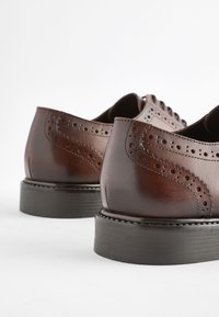 Brown leather shoes featuring decorative broguing, a smooth finish, and a thick black rubber sole for added durability and traction.