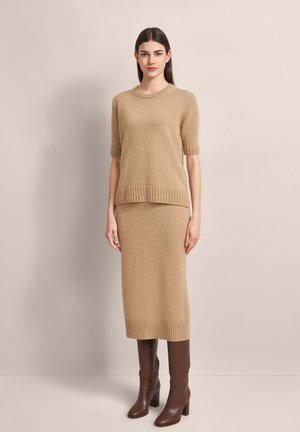Knit beige sweater and skirt set with ribbed hems, featuring short sleeves, a round neckline, and paired with brown knee-high heeled boots.