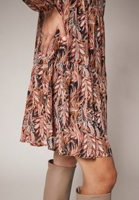 Robe à motif floral avec des nuances d'orange et de noir, dotée d'une jupe en cascade et d'une texture de tissu léger.