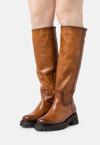 Bottes montantes en cuir marron avec une finition lisse, détail zippé et talon noir empilé. Présentent un design à bout arrondi et une semelle robuste.