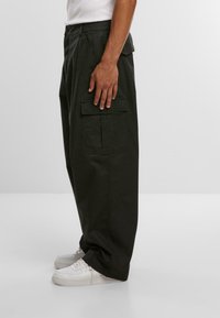 Schwarze Cargo-Hosen mit lockerer Passform, ausgestattet mit Seiten- und Gesäßtaschen. Hergestellt aus strapazierfähigem Stoff, kombiniert mit weißen Sneakern.