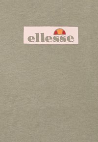 Ljus olivgrön t-shirt med en rektangulär rosa logotyp som visar "ellesse" och en färgglad halvcirkel, gjord av mjukt bomullsmaterial.