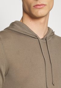 Brun texturerad hoodie med dragsko, med en avslappnad passform och ribbade muddarna. Tyget har ett subtilt, vävt mönster.