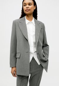 Hall hallitsetud ülikond terava kraega jopet, ühe tasku ja sobivate pükstega valge nööbitava särgi peal. Siidine tekstuuriga kangas.