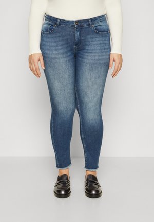 Jeans skinny in denim blu, con tasche frontali, chiusura con bottone e orlo sfrangiato. Abbinati a mocassini neri lucidi.