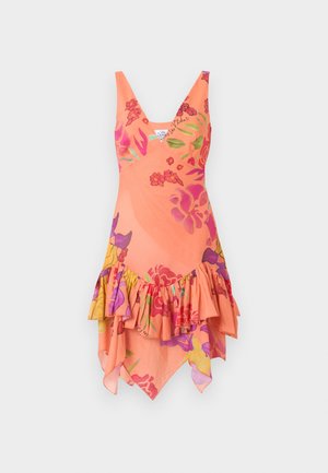 Γυναίκα που φοράει κοραλί αμάνικο φόρεμα με V λαιμόκοψη, λουλουδάτα σχέδια και ασύμμετρο βολάν στο τελείωμα, συνδυασμένο με γυμνά σανδάλια ψηλοτάκουνα.