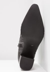 Chaussure noire à bout pointu avec semelle texturée, talon bloc, et taille 37 visible sous la chaussure.