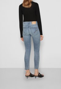Jeans ajustados en denim azul claro, con cintura alta, bolsillos traseros y un parche de cuero en la parte trasera. Combinados con mule negros de tacón.