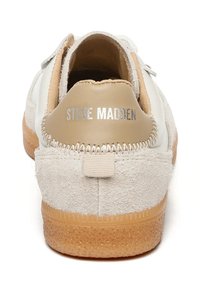 Sneaker bianca e beige realizzata in materiali scamosciati e in pelle, con una suola in gomma beige, dettagli cuciti e il marchio "Steve Madden" sul tallone.