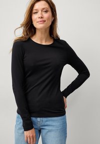Sort langærmet tætsiddende top i et glat, let stof med rund halsudskæring, parret med lyseblå denimjeans.