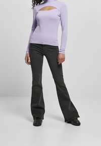 Světle fialový dlouhý rukáv top s oblé výstřihem na hrudi, spárovaný s černými rozšířenými džíny a černou obuví.