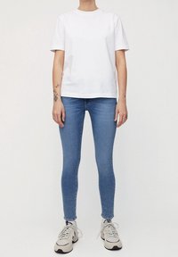 Vit bomull t-shirt med korta ärmar, tillsammans med ljusblå skinny jeans och beige sneakers med grå accenter.