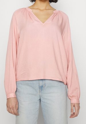 Helle pinkfarbenes langärmliges Blusenshirt mit V-Ausschnitt, gerafften Details am Kragen und elastischen Bündchen. Getragen mit hellblauen Jeans.