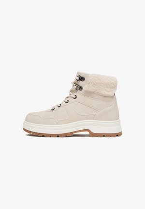 Bota de invierno beige hasta el tobillo con cordones en la parte frontal, cuello de piel sintética, suela gruesa blanca y suela exterior marrón con dibujo para tracción.