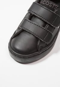 Černá syntetická bota s kulatou špičkou, suchými zipy a texturovaným svrchním materiálem. Má gumovou podrážku a prošívání podél okrajů.