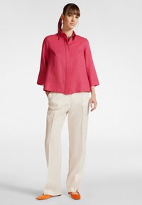 Camicia di lino rosa con colletto, maniche a tre quarti e vestibilità ampia, abbinata a pantaloni beige a gamba larga e scarpe arancioni slip-on.