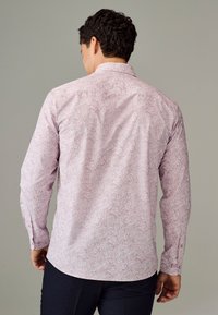 Camicia a maniche lunghe in rosa chiaro con intricati motivi floreali bianchi. Presenta un colletto standard e un orlo curvo. Tessuto morbido e liscio al tatto.
