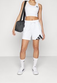 Vit sportbh och shorts med svarta accenter, parat med vita strumpor och sneakers. En svart crossbody-väska finns också med.