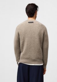 Beżowy wełniany sweter o miękkiej fakturze, z okrągłym dekoltem i ściągaczem na dole. Posiada małą czarną metkę z tyłu przy szyi.