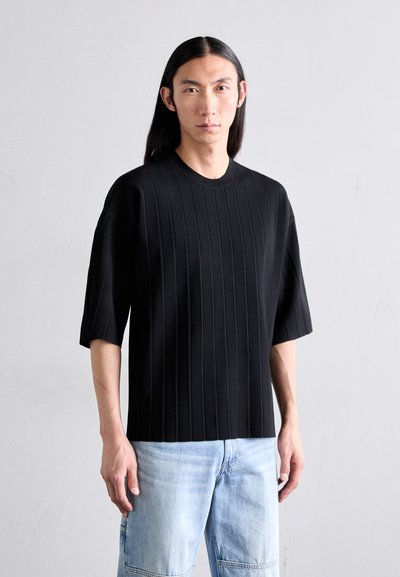 T-shirt noir à manches courtes avec texture à côtes verticales et col rond, associé à un jean en denim bleu clair.