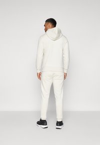 Cream-colored sweatshirt with a hood and matching sweatpants. Simple, soft fabric; fitted cuffs; worn with black athletic shoes.