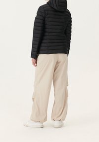 Czarna pikowana kurtka puchowa z poziomym wzorem pikowania i kapturem, zestawiona z luźnymi beżowymi spodniami typu cargo oraz białymi tenisówkami.