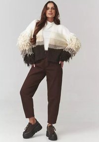 Szydełkowy kardigan z długimi, frędzlami; gradient od kremowego do brązowego. Połączony z brązowymi spodniami z wysokim stanem i masywnymi czarnymi butami.