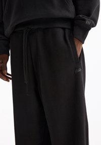 Schwarze, locker sitzende Sweatpants aus weichem Stoff mit einem verstellbaren Kordelzug, Seitentaschen und einem dezenten Logo-Element nahe dem Saum.