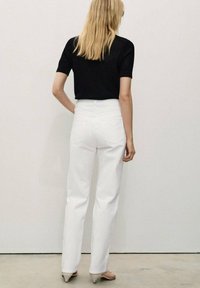Top corto nero a maglia con maniche corte abbinato a jeans bianchi a gamba dritta a vita alta, con dettagli sul retro e una texture liscia.