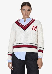 Maglione lavorato a maglia color crema con scollo a V profondo e una fascia a righe rossa e nera. Presenta un logo "M" sul petto e un motivo testurizzato.