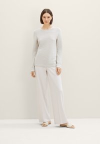 Pull à manches longues côtelé gris clair avec un col arrondi, associé à un pantalon large blanc et des sandales beiges à enfiler.