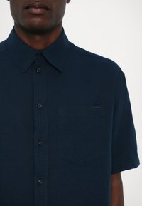 Navy Kurzarmhemd aus strukturiertem Stoff, mit durchgehender Knopfleiste, spitzem Kragen und einer kleinen Tasche mit gestickten Details.