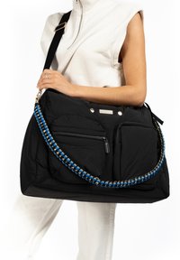 Large black bag with quilted texture, featuring two front pockets and a blue and gold chain strap. Zipper detail and metallic accents present.
