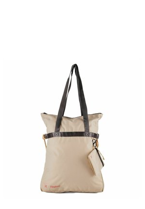 Beige Haglöfs draagtas met zwarte handvatten, ritssluiting bovenaan en een klein zakje aan een clip bevestigd, weergegeven op een witte achtergrond.