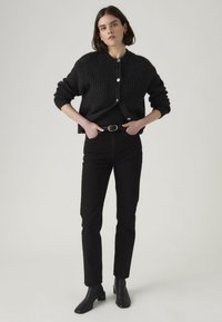 Black ribbed knit cardigan with round neckline, button closure, and long sleeves, paired with black jeans and ankle boots. Simple design.