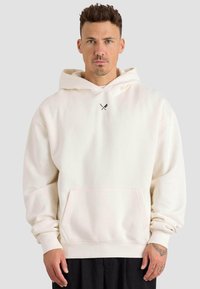 Sudadera de color crema claro en tejido suave, con un bolsillo tipo canguro y puños acanalados. Pequeño diseño gráfico en el pecho. Corte casual.