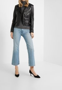 Svart skinnmotorcykeljacka med dragkedjefickor, grå stickad polo, ljusblå utsvängda jeans och svarta spetsiga klackskor.